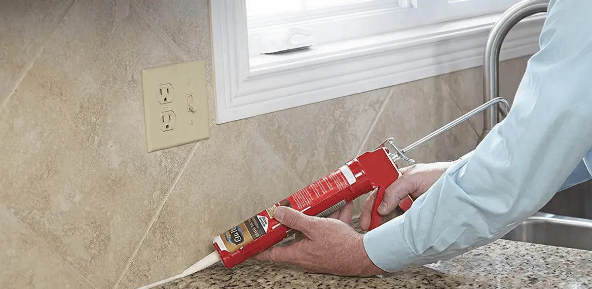 Handyman applying caulk along a kitchen backsplash and countertop seam in Ann Arbor, MI